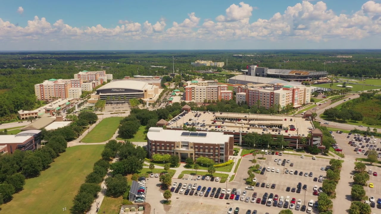 Ripresa aerea dell'area del campus est della UCF a Orlando, che mostra la CFE Arena, gli alloggi per studenti, le mense e ampi parcheggi circondati da una vegetazione lussureggiante