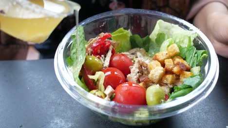 person pouring dressing over a chicken salad