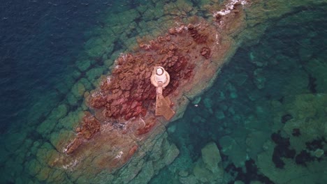 Breathtaking-top-down-aerial-of-lighthouse-on-rocky-offshore-island,-zoom-out