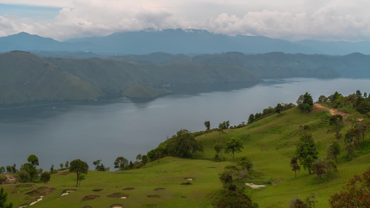 Panoramic view of a large lake surrounded by green hills, with a golf course in the foreground