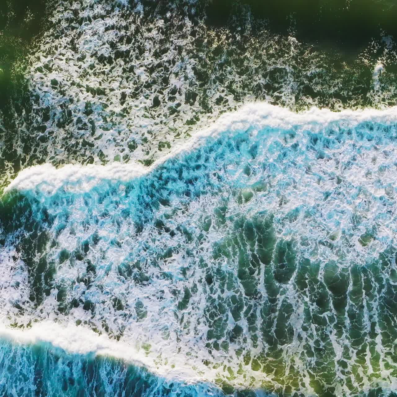 Green waters of the beautiful ocean with quickly moving waves. Following the foamy waves moving to the shore. Top view