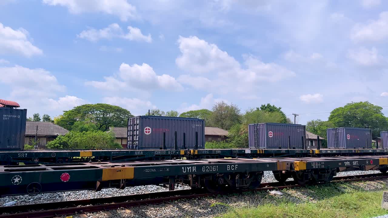 Daytime freight train passes empty rural railway station platform under bright sky, handheld tracking shot