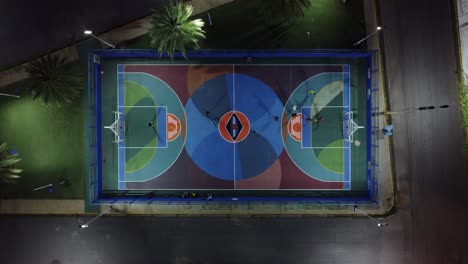 aerial zenithal night view of people playing indoor soccer on a colorful field in the middle of a city