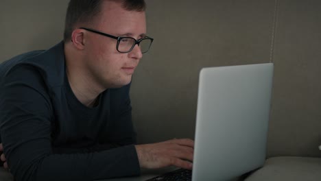 man with down syndrome using laptop at home while lying on sofa.