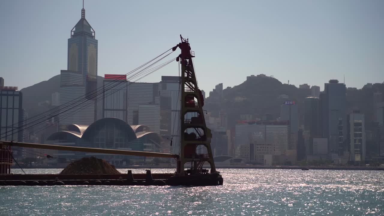 홍콩의 빅토리아 항구에서 항해하는 큰 건설 크레인 보트, 은 푸른 하늘의 여름 날, 물 위에서 반사되는 빛.