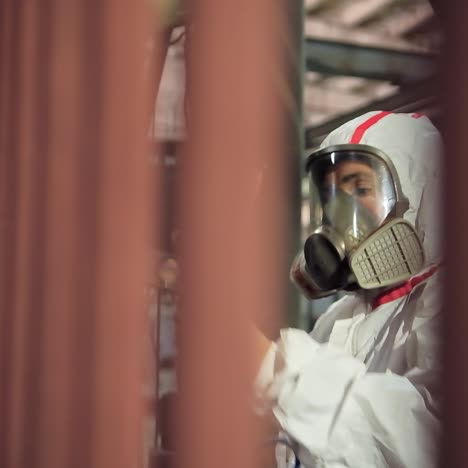 painting process in workshop. a man in safety suit and respirator paints metal frame with a spray gun inside the small factory.