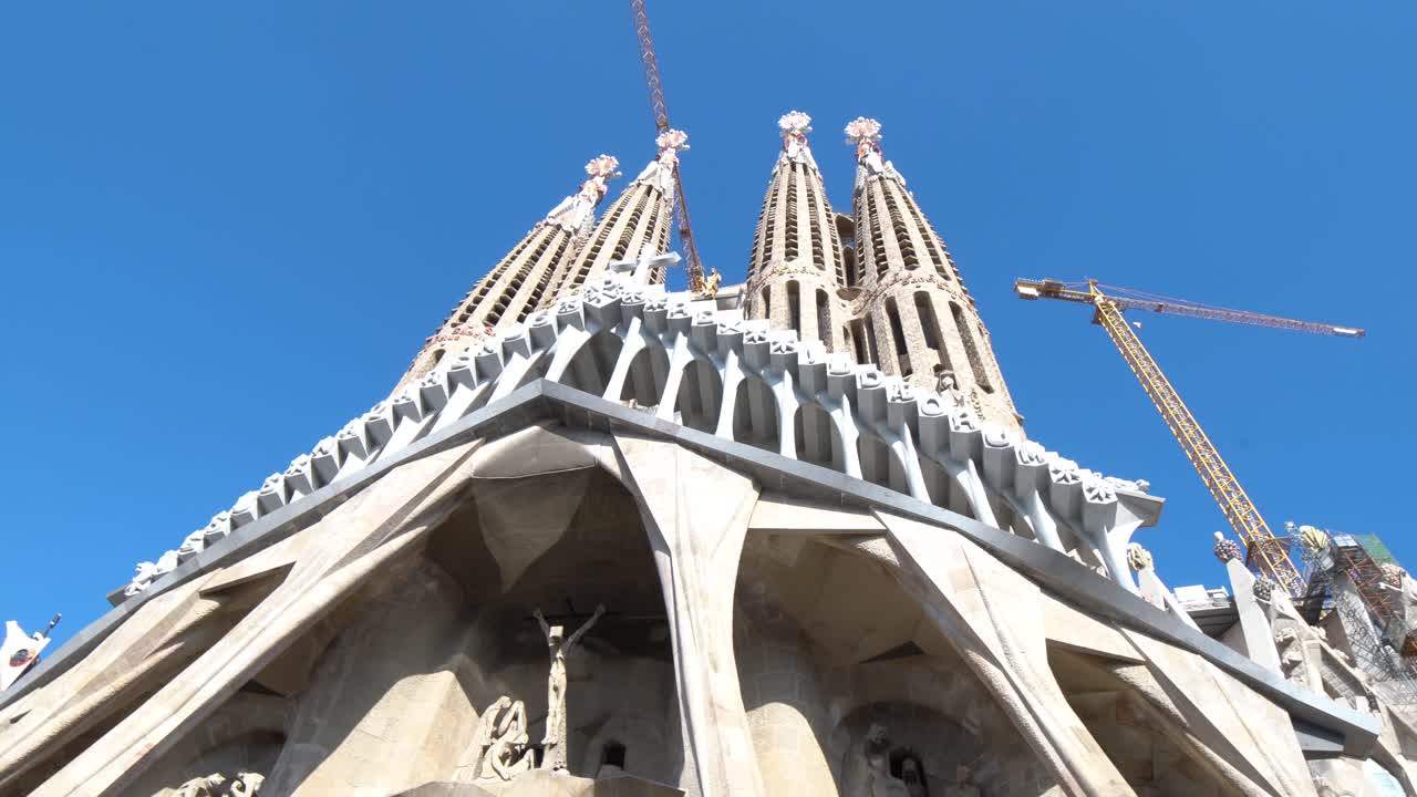 Upwards look at the Christ Facade with blue sky at La Sagrada Familia with construction cranes, Barcelona