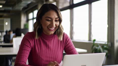 happy young hispanic businesswoman working on laptop in modern office
