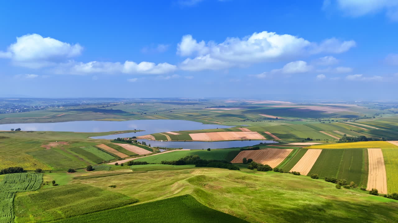 Vast rural landscape. Vast fields stretch across the terrain under a bright blue sky, featuring varying shades of green and yellow crops