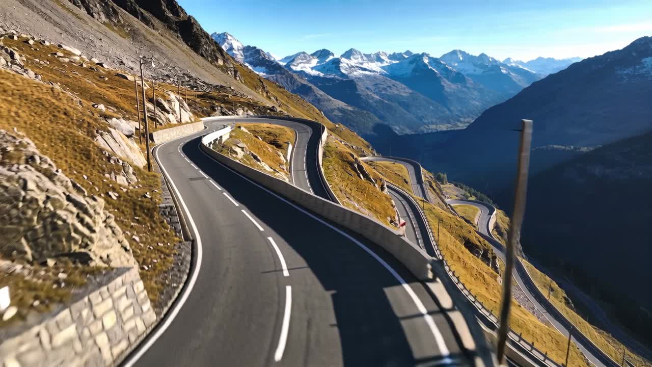Drone em descida revelando estrada de asfalto sinuosa em alta passagem de montanha, mostrando guarda-corpos e picos