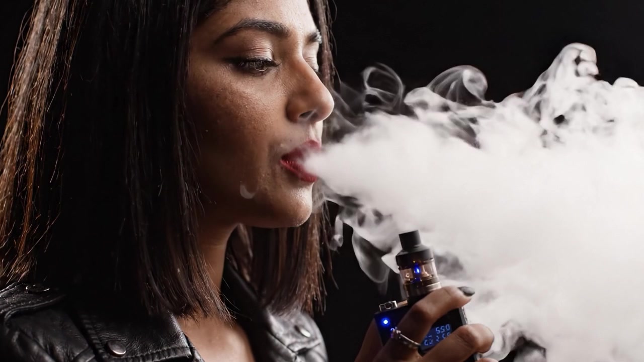 Striking Portrait of a Stylish Individual Holding a Vape Device Against a Dark Background, Highlighting Modern Lifestyle Choices and Individual Expression