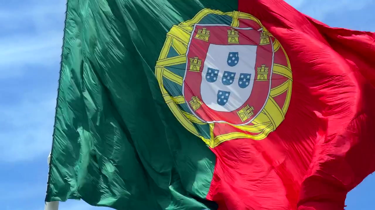 Bandera portuguesa ondeando contra un cielo azul claro.