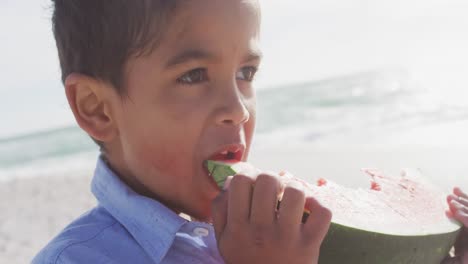 Porträt-Eines-Glücklichen-Hispanischen-Jungen,-Der-Am-Strand-Wassermelone-Isst