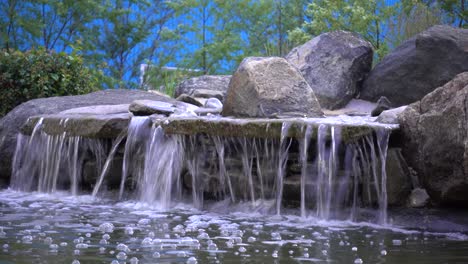 cascada de roca con árboles en el fondo y un poco de viento