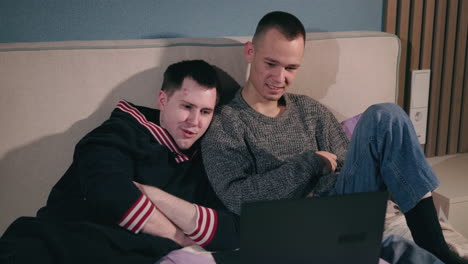 two men watching laptop on bed