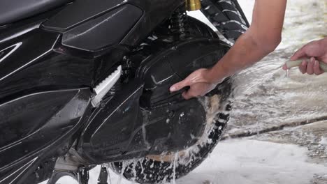 person washing and rinse motorcycle wheel with water pipe, soapy water on floor