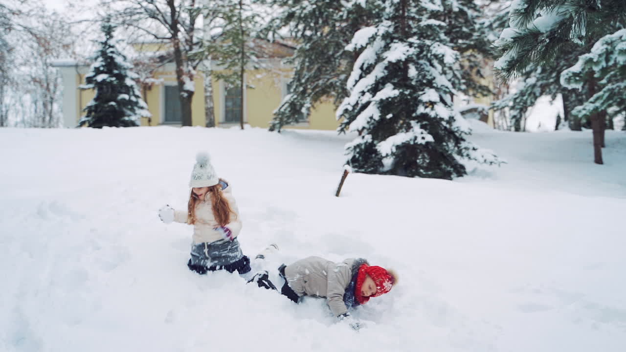 Two little girls crawling in the snow on the forest background in winter. Happy children are playing in soft white snow outdoors. Slow motion.
