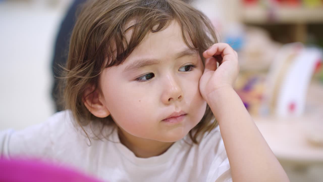 Young Ukrainian white toddler curiously using a drawing tablet, sitting with engaged expression in slow motion looking off into distance, close up