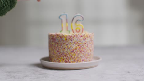 studio shot birthday cake covered with decorations and candle celebrating sixteenth birthday being lit