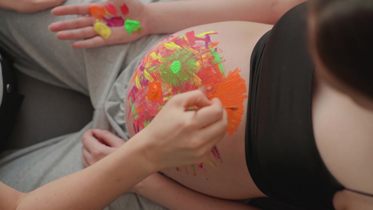 Mani che dipingono arte astratta colorata sul ventre di una donna incinta