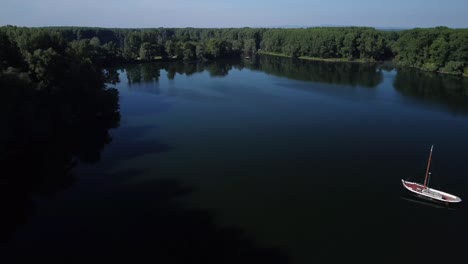 Drone-flying-sideway-until-yacht-comes-into-view-on-a-quiet-river-in-Germany-at-sundown