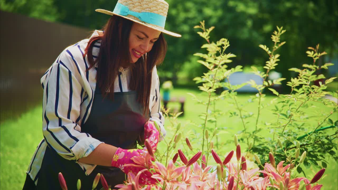 Woman in striped shirt and hat tending to vibrant flowers in a sunny garden setting