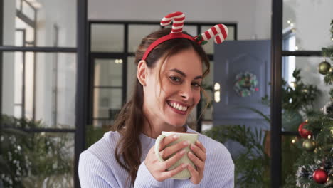 smiling woman wearing festive headband enjoying hot drink at home during christmas
