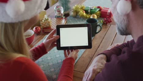 Glückliches-Kaukasisches-Reifes-Paar-Mit-Weihnachtsmützen-Und-Tablet-Mit-Kopierplatz