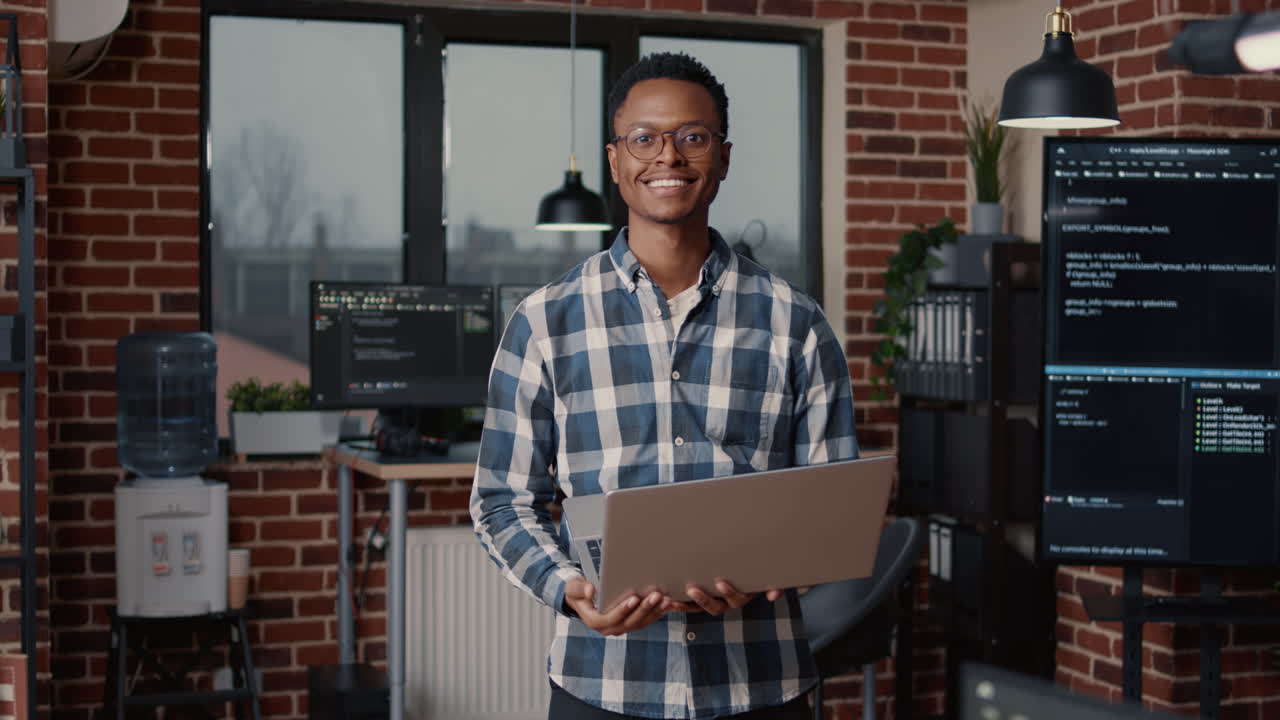 Portrait of african american programer standing working on laptop looking up and smiling