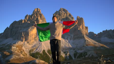 imágenes filmadas en rifugio auronzo, tri cine en las montañas de los dolomitas italianos con un hombre moviéndose y sosteniendo una bandera italiana y con hermosas montañas en el fondo, filmadas al amanecer en 4k