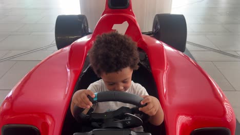 3 year-old black kid driving in a red f1 toy car