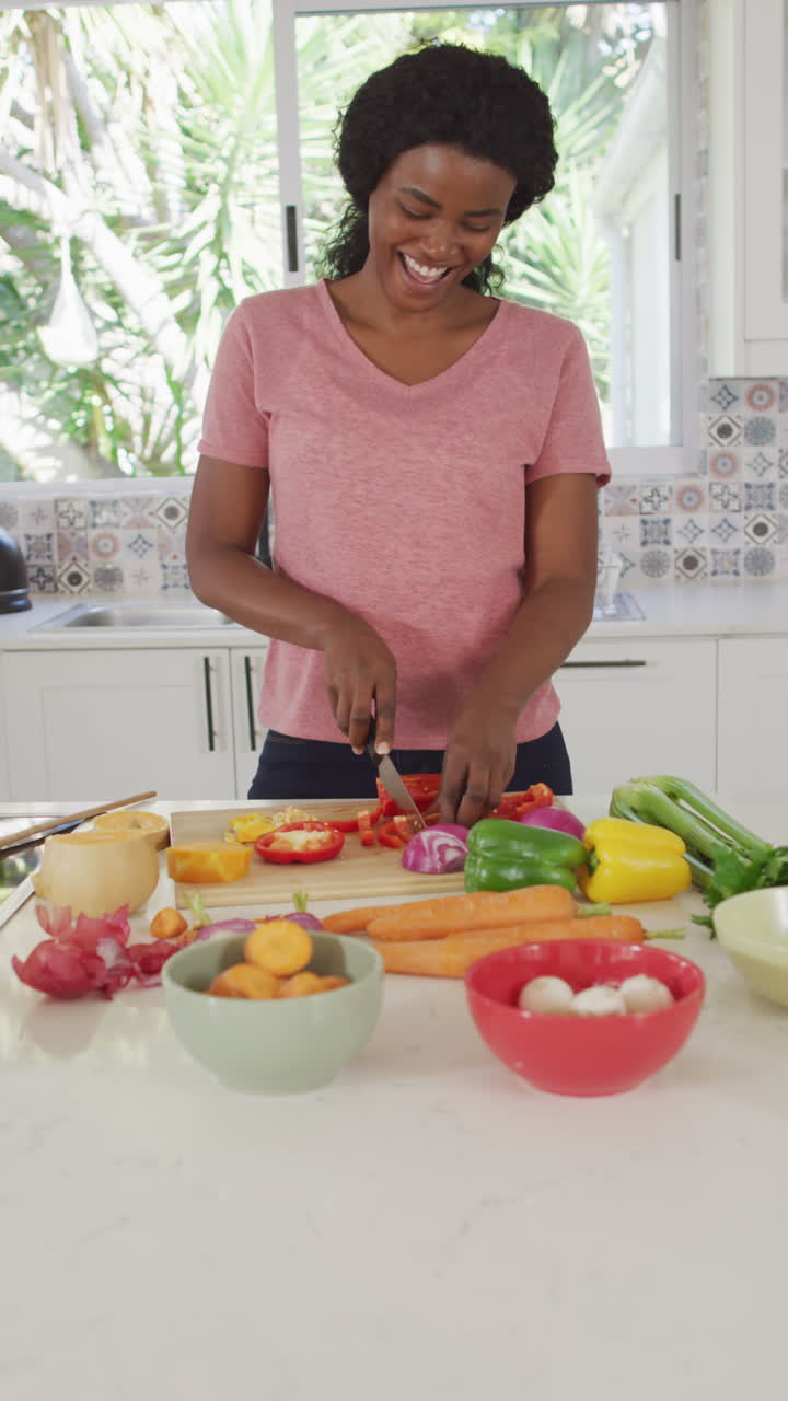 Vídeo vertical de mulher afro-americana feliz preparando uma refeição na cozinha