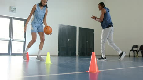 dribbling basketball around cones, woman training on indoor court with coach
