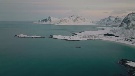 Aerial-view-over-frozen-Ramberg-lake-towards-snowy-glacial-Scandinavian-peaks