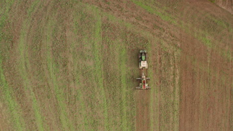 top down aerial follow shot over a green tractor ploughing a field