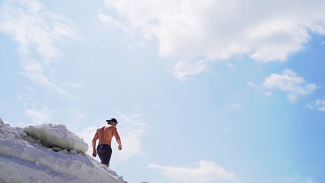 shirtless man going down the hill. back view of muscular sportsman in the mountains under blue sky. view from below. slow motion.