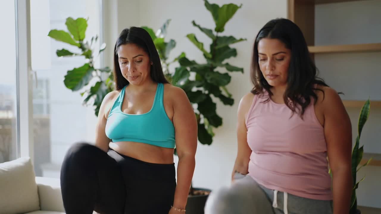 Due donne che alzano e abbassano le braccia, iniziando a marciare ed eseguendo sollevamenti delle ginocchia per il fitness vicino alla finestra.