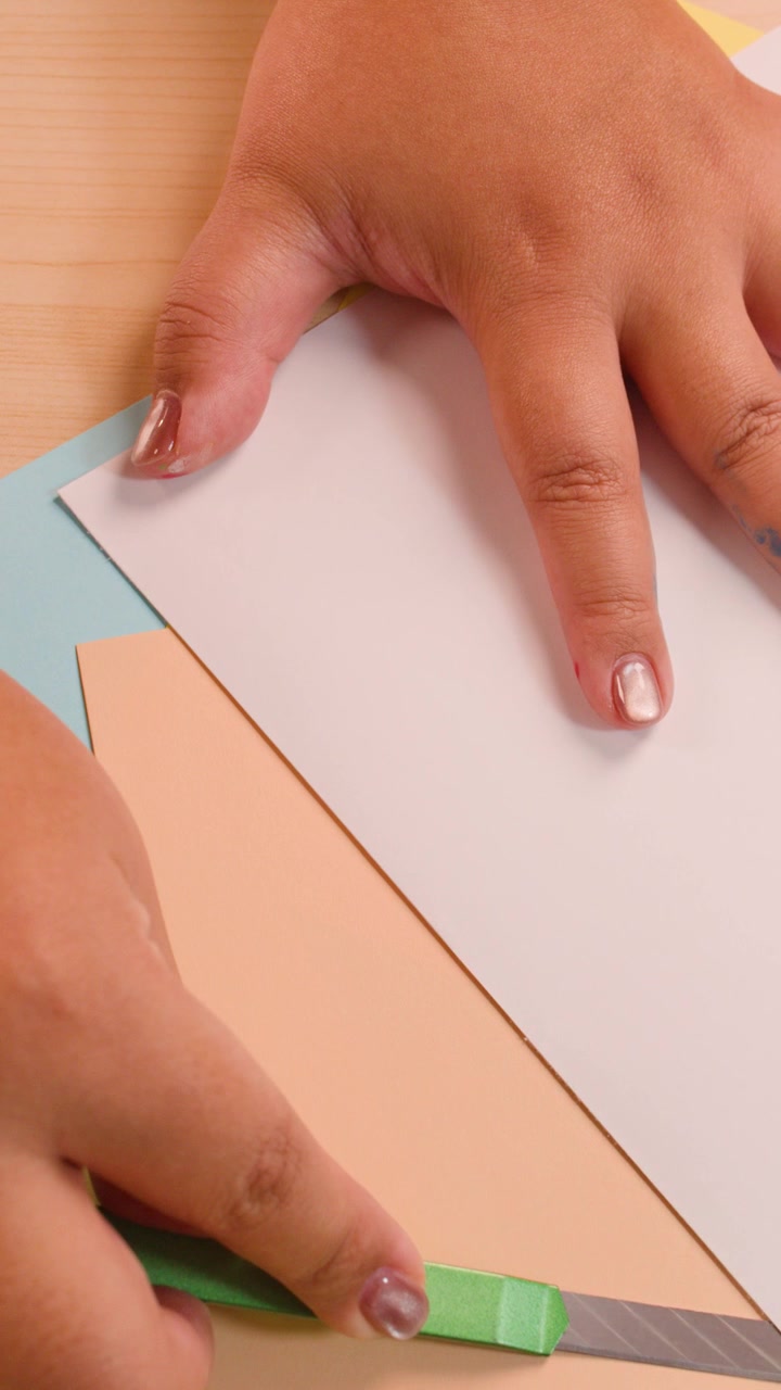 Hands cut and fold colored paper on desk under soft lighting, top-down camera angle throughout