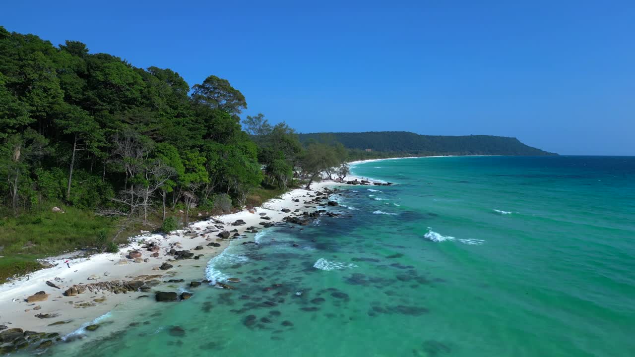 Black Stones in turquoise water gently washing the white sand beach of Koh Rong island, cambodia, on a sunny day with clear blue sky. Nice aerial view flight overflight flyover drone