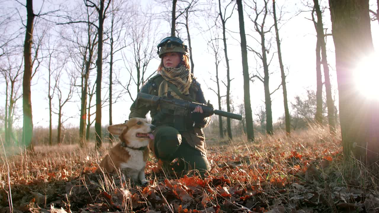 joven pelirroja bonita en uniforme militar armada con un rifle jugando con el perro