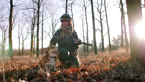 joven pelirroja bonita en uniforme militar armada con un rifle jugando con el perro