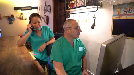 panning shot of doctor and nurse on the computer and telephone at reception of the clinic