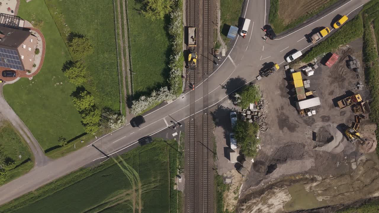 Top-down drone shot of a construction site at a railway crossing in Unna, Germany. Roadworks and vehicles near railway tracks on a sunny spring day.