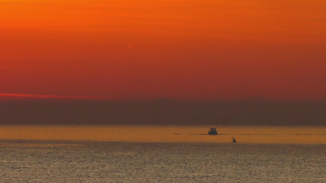 주황색 새벽 하늘 아래 잔잔한 바다에서 낚시 보트와 카약