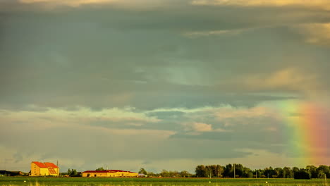 geniales lapsos de tiempo de un arco iris y nubes moviéndose en el cielo sobre un camino en una granja