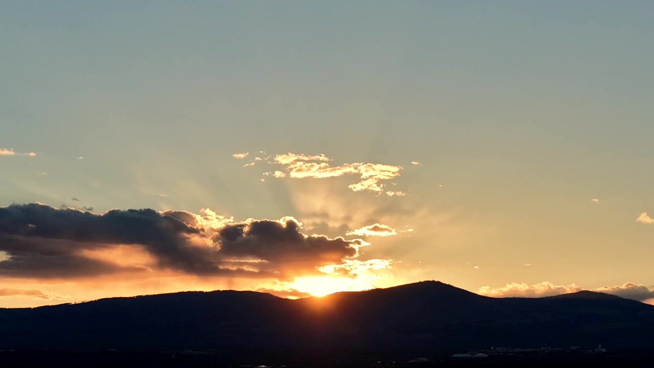 Timelapse 4K con drone cattura il tramonto tra nuvole in movimento e una silhouette montuosa frastagliata. Movimento atmosferico cinematografico mentre la luce dell'ora d'oro svanisce su un vasto paesaggio sud-occidentale.