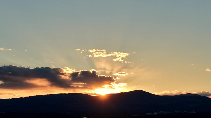 Timelapse 4K con drone cattura il tramonto tra nuvole in movimento e una silhouette montuosa frastagliata. Movimento atmosferico cinematografico mentre la luce dell'ora d'oro svanisce su un vasto paesaggio sud-occidentale.