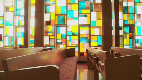 dolly shot of rows of empty church pews framed by a stunning stained glass window wall blossoming with vibrant colors