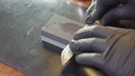 hands in black gloves sharpen kitchen knife on wet whetstone on table