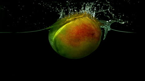 mango cayendo en el agua sobre un fondo negro